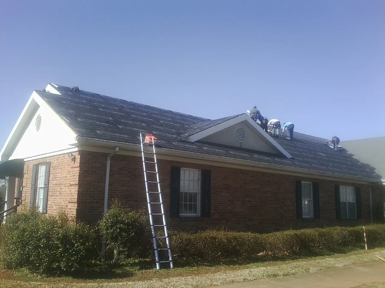 Crew tearing shingles off a brick ranch roof with a ladder set — Emergency Roof Repair work by our crew in Immaculata