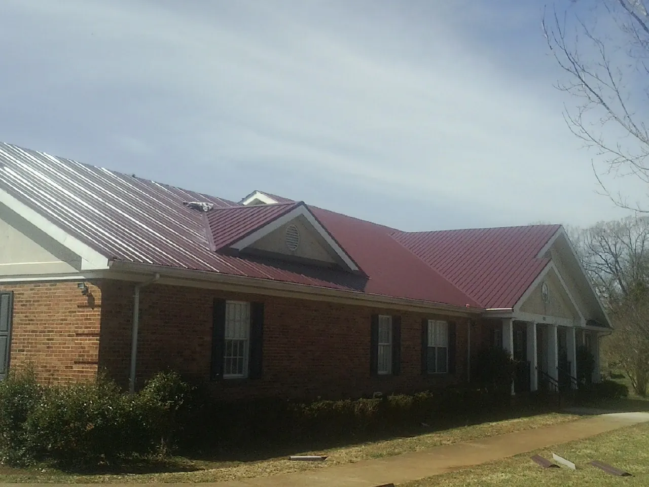 Red metal roof with gabled entries on a long brick building, from a Hail Damage Roof Repair job in Immaculata