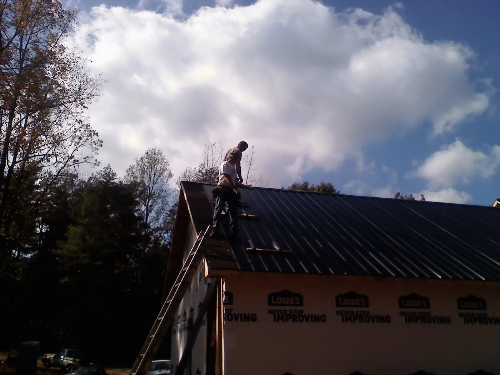 Roofer fastening dark metal panels high against a cloudy sky, from a Roof Inspection job in Immaculata