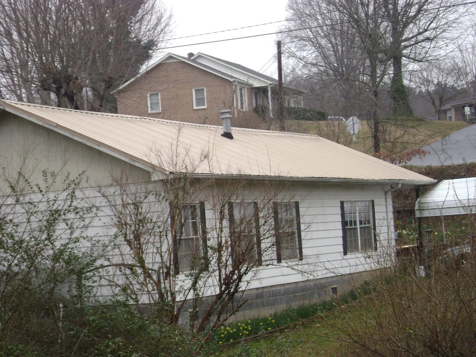 Tan metal roof on a white sided house set into a hillside — Commercial Roofing by Roofing Brothers in Immaculata